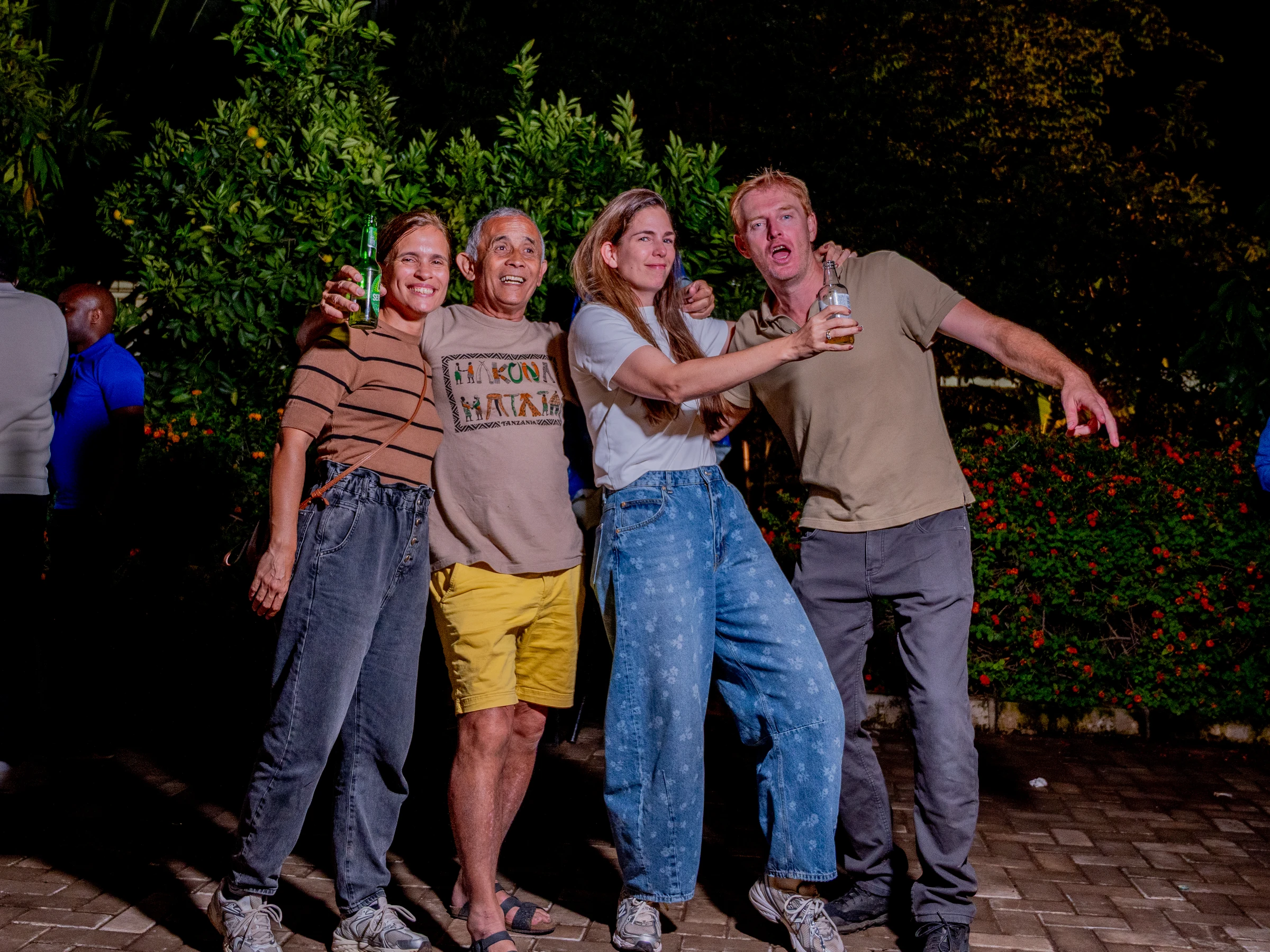 Four guests posing together beside greenery at night